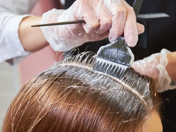 A stylist applying hair color to roots